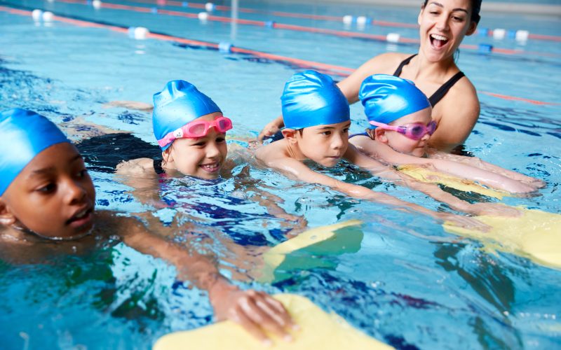 Female,Coach,In,Water,Giving,Group,Of,Children,Swimming,Lesson